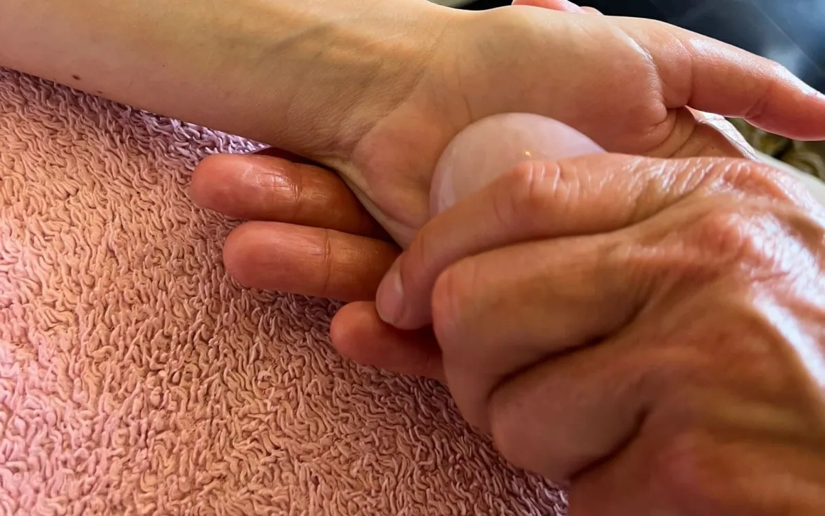 Seniorenmassage: Jolanda masseert met een rozenkwarts steen de hand van een oudere cliënt