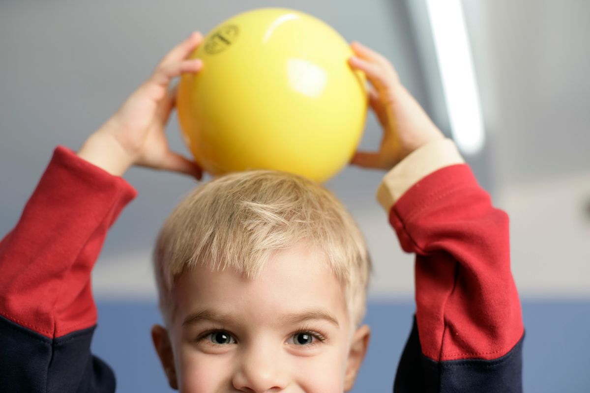 Lachend kindje dat een grote gele bal boven zijn hoofd houdt